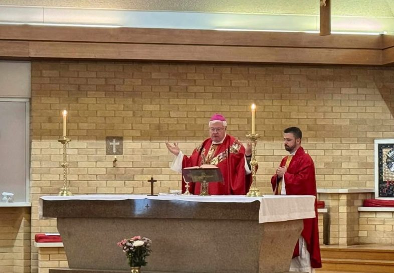 Archbishop Charles Balvo celebrating Mass at the chapel altar in red vestments
